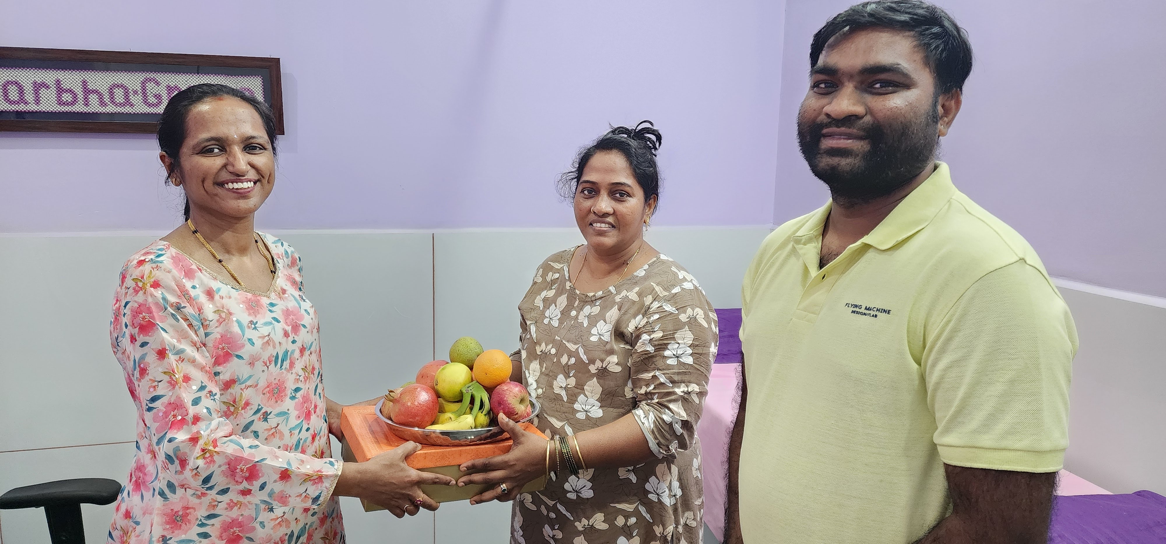 Grateful couple presenting a fruit basket to Dr. Rashmi T N at GarbhaGruha Health Center